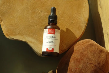 flacon d'huile de baobab, couché sur une plateau en bois avec une coque du fruit du baobab